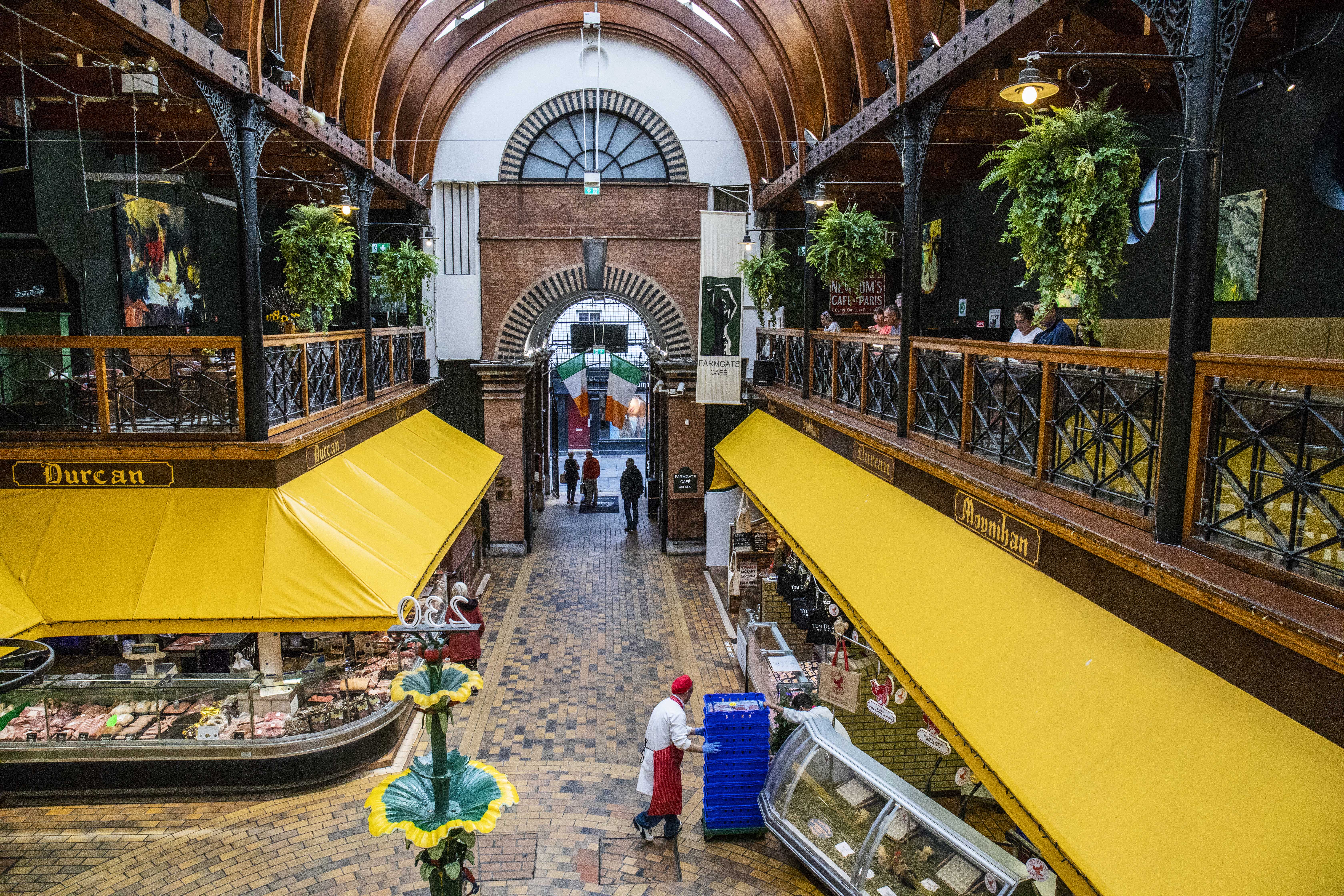Interior of Cork's English Market with yellow stall awnings, the central fountain and Farmgate Caf&eacute; above.